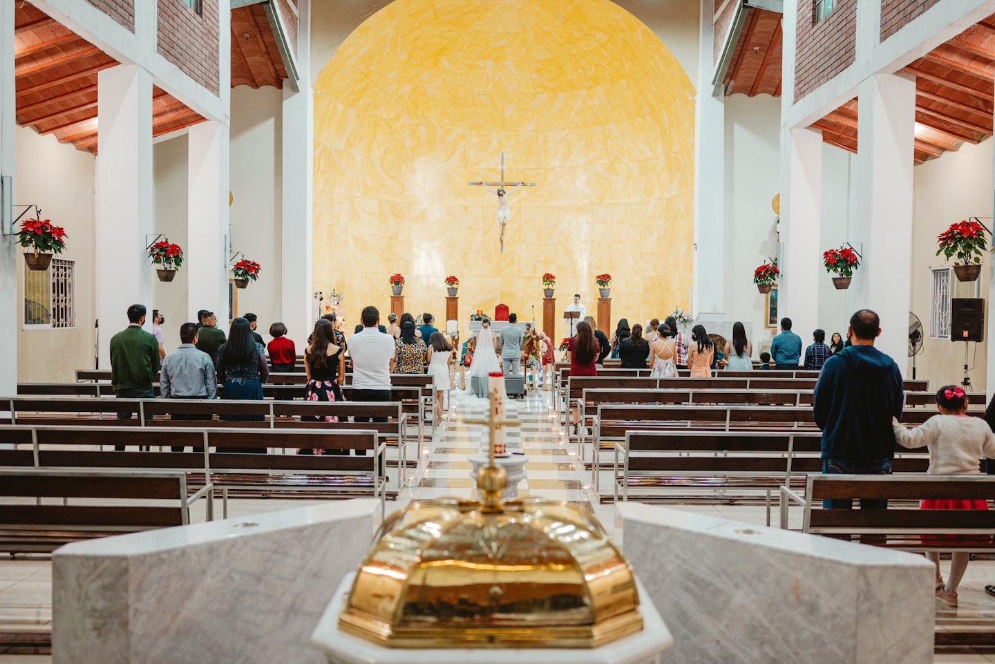 Congregation sits in pews facing a large crucifix on a wall.