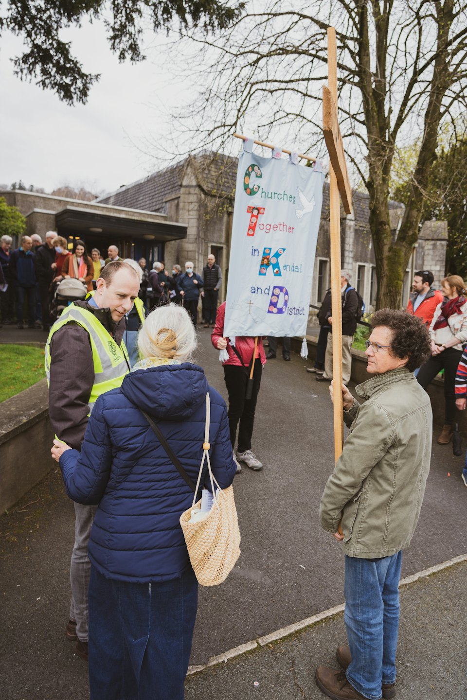 People gather outside a stone church holding a community banner.