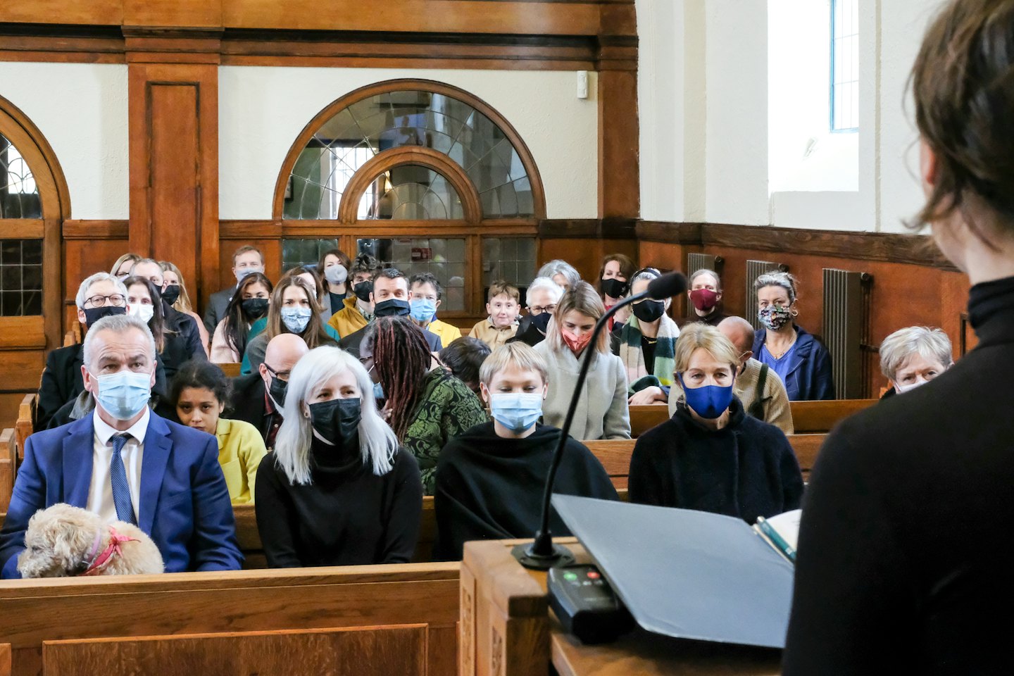 People in masks listen to a speaker in a wooden church.