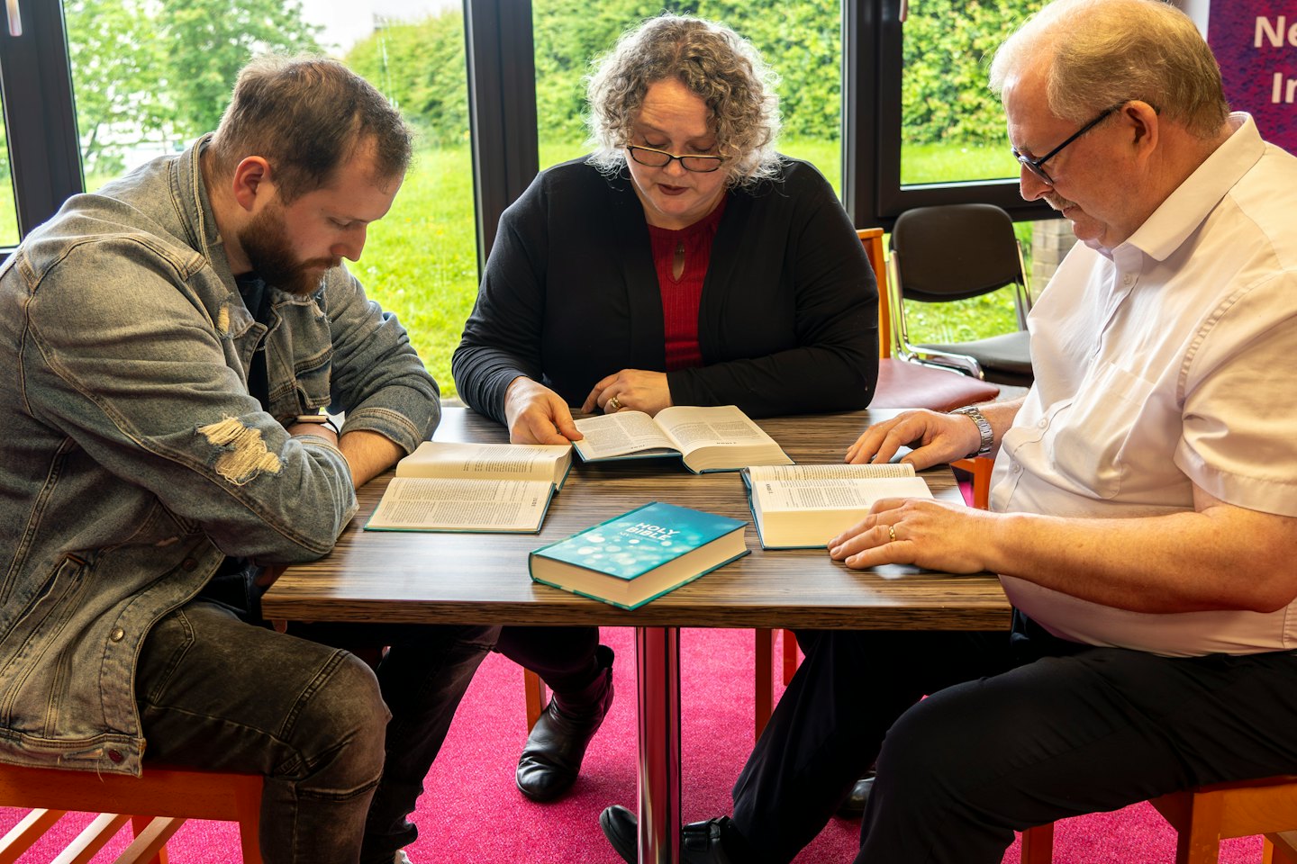 Three people study the Bible around a wooden table.