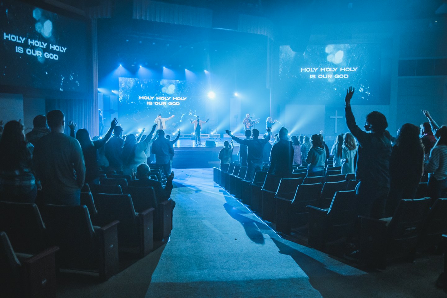 Audience with hands raised during a worship service with text on screens.